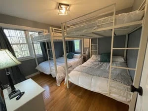 Clean master bedroom with two beds, hardwood floors, windows, and organized workspace
