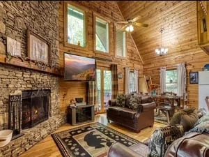 Rustic log cabin living room with exposed wood beams, brick fireplace, and hardwood flooring