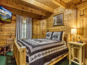 Clean log cabin bedroom with wood walls, exposed beams, and neatly made bed with patterned bedding